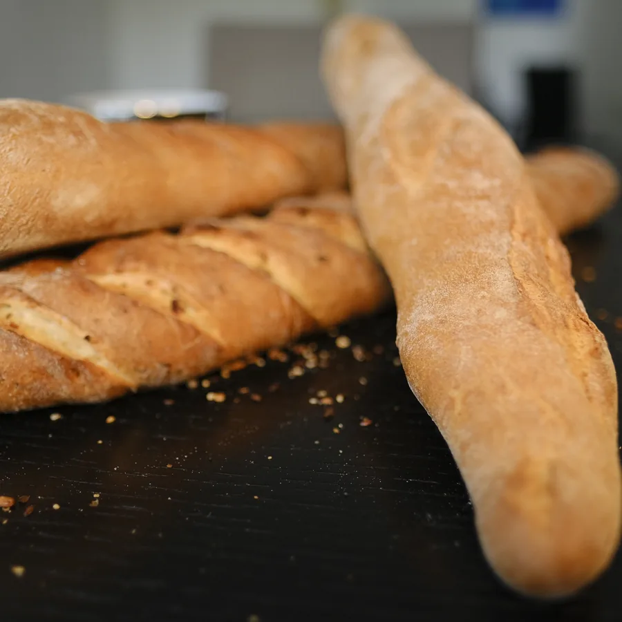 Drei Baguettes mit heller Kruste auf einer dunklen Arbeitsfläche.