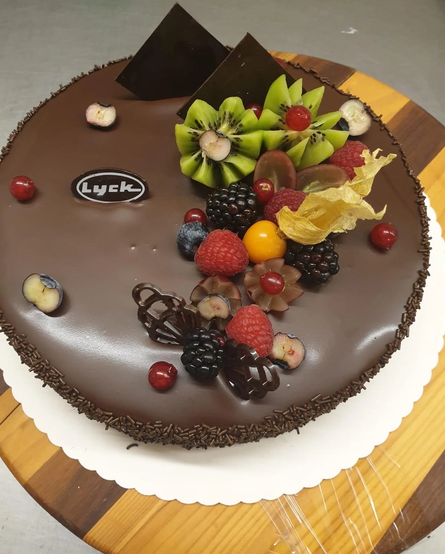 Eine Schokoladentorte mit Lyck-Plakette, belegt mit Himbeeren, Brombeeren, Kiwi und Physalis.
