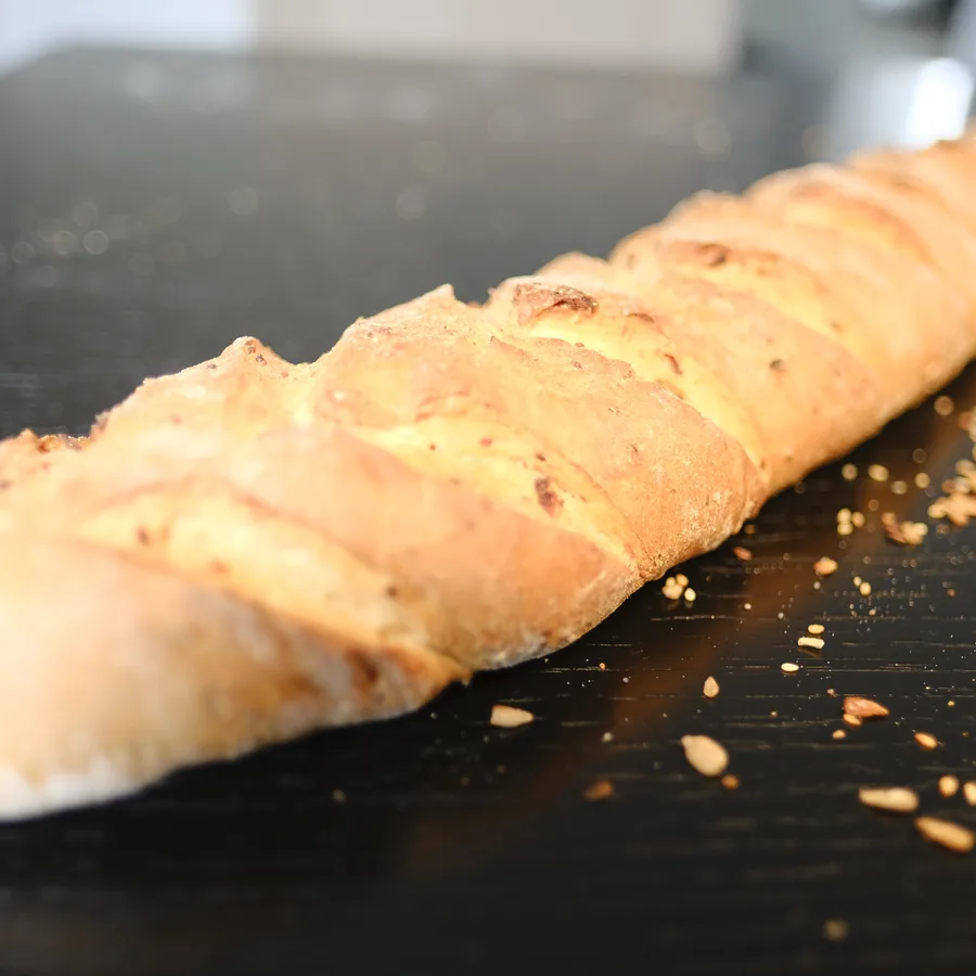 Ein eingeschnittenes Baguette mit Saaten auf dunklem Holz.