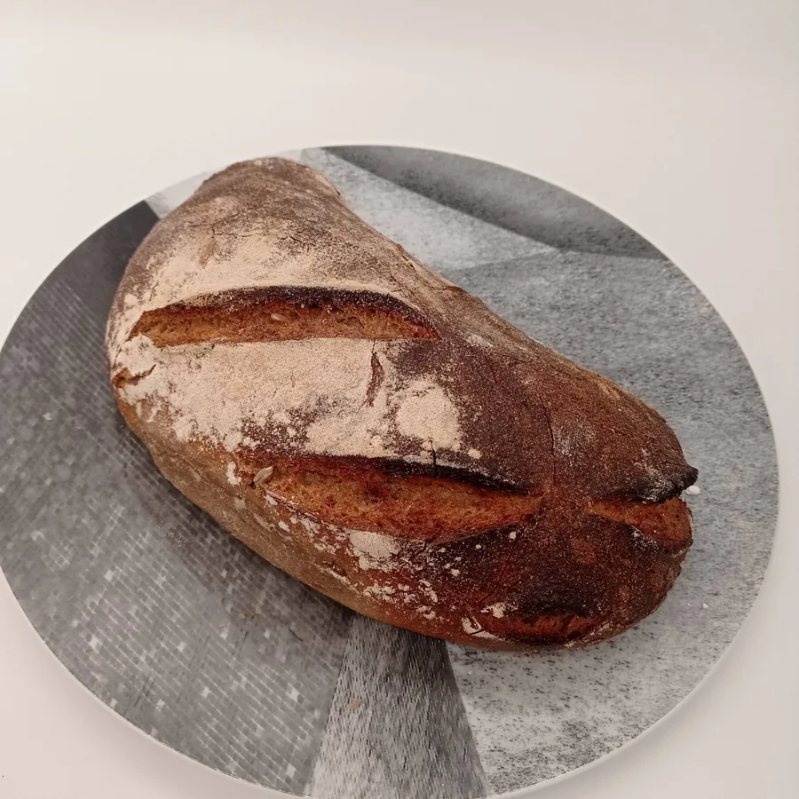 Ein dunkel ausgebackener Brotlaib mit bemehlter Kruste und tiefen Einschnitten.