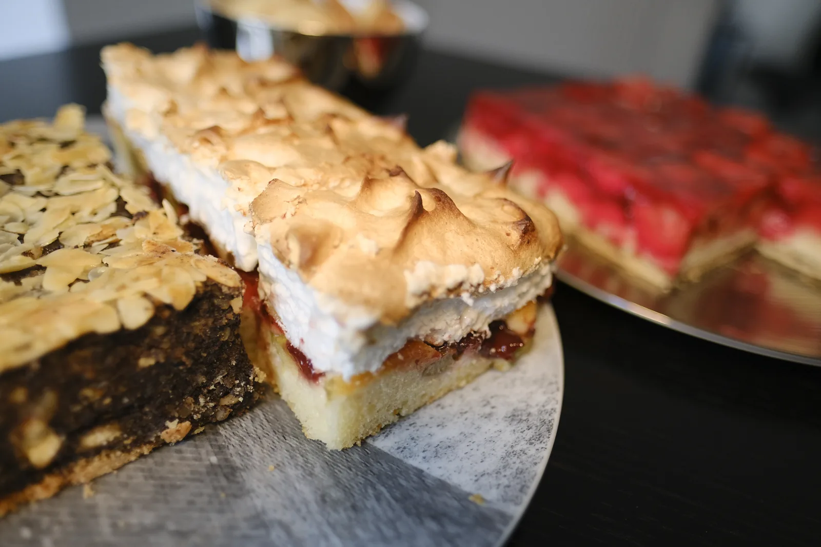 Drei Stücke Blechkuchen nebeneinander: Mohn mit Mandeln, Kirsch mit Baiser und Erdbeer.