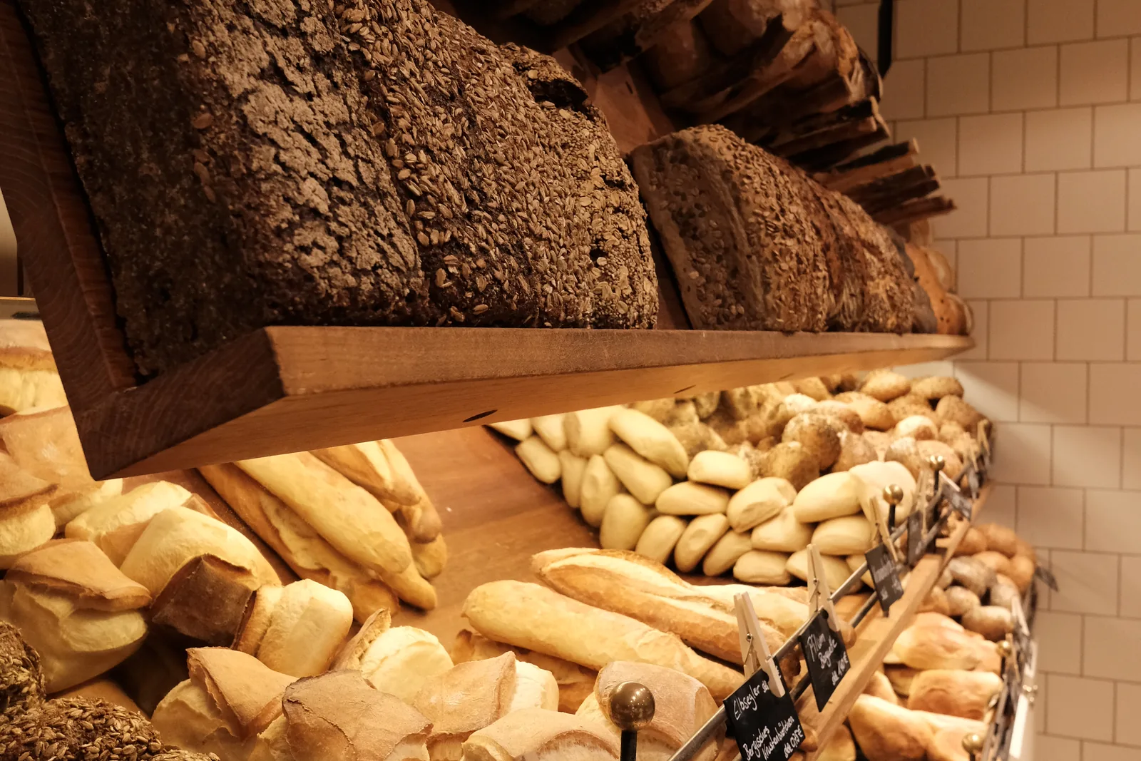 Blick in die Auslage: Brote im Holzregal, darunter Brötchen und Gebäck in Körben.